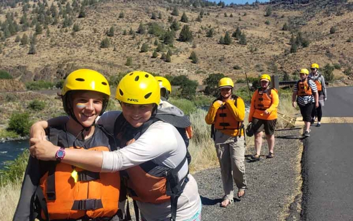 two students embrace in the foreground while others trail behind on a rafting expedition with outward bound